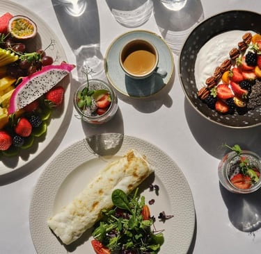 Healthy breakfast spread with fruit platter, yogurt bowl, egg wrap, and coffee in morning sunlight.
