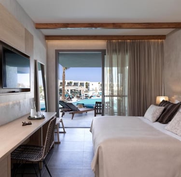 Modern luxury hotel room with wood beams, queen bed, and balcony overlooking a resort swimming pool.