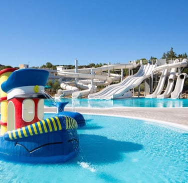 Family water park with colorful boat fountain and multi-lane water slides at a sunny resort.