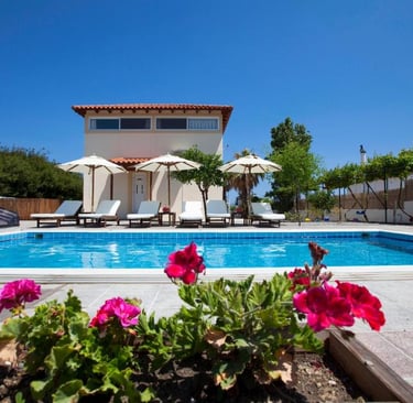 Luxury vacation villa with private swimming pool, sun loungers, and patio umbrellas under a clear blue sky.