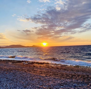 Golden sunset over a rocky pebble beach with ocean waves and a blue cloudy sky.