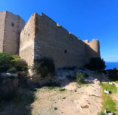 Medieval stone castle ruins overlooking the deep blue Mediterranean Sea under a clear sky.