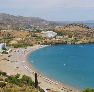Aerial view of a sandy beach cove with luxury resorts and blue ocean water in Rhodes, Greece.
