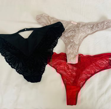sexy panties laid out on soft bed - black sued panties, a beige flowery thong and a red lace thong