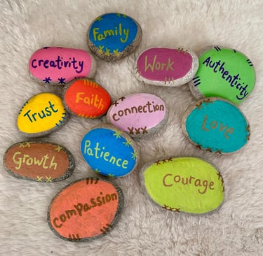 Therapy stones with values words painted on colourful backgrounds, placed on a furry surface.