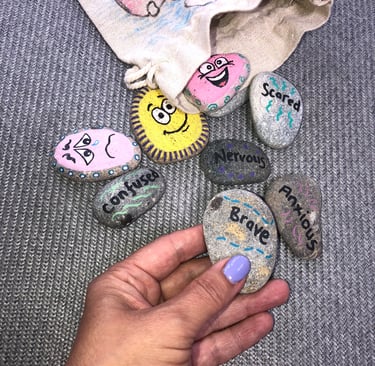 A selection of hand-painted therapy stones. One stone is being held, it says 'brave'. 