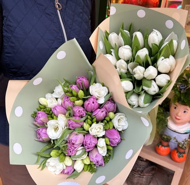 Fresh bouquets of white tulips and purple blossoms wrapped in polka dot paper for a floral gift.