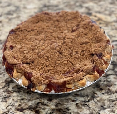 Freshly baked peach crumble pie with a golden brown streusel topping on a granite countertop.