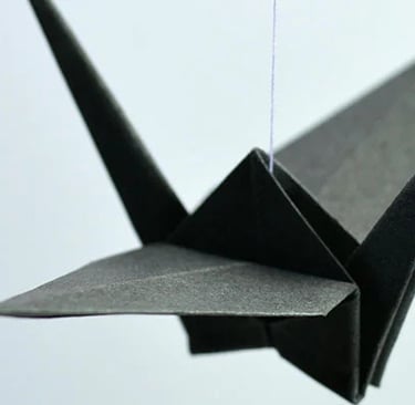 Una gru nera fatta con gli origami su sfondo azzurro