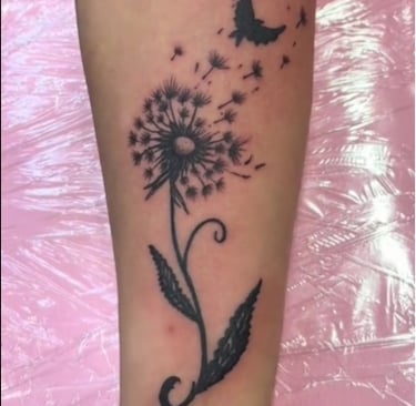 a tattoo of a dandelion flower on a woman's forearm