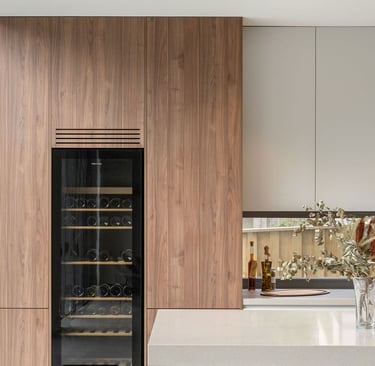 Nowoczesna jasna kuchnia. W wysokiej szafce zamontowana przeszklona lodówka na wino