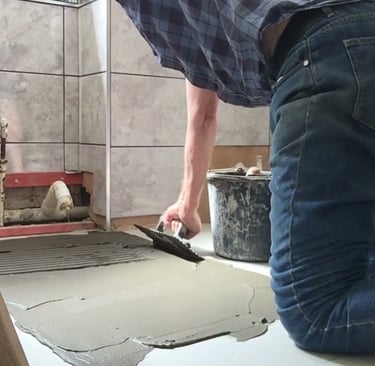 Pracownik rozkłada klej na podłodze, za pomocą grzebienia. 