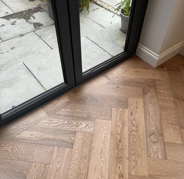 A brown oak herringbone floor with a border against folding doors