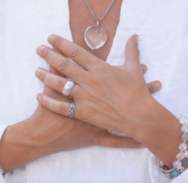 a woman in a white shirt with her hands across her heart wearing silver jewelry