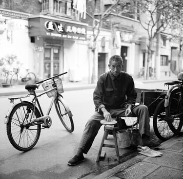 Man sits on a street in Shanghai sharpening his knives with a grindstone