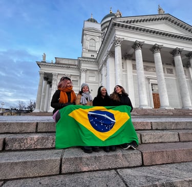 Quatro fundadoras do BiF sentadas na escadaria da Catedral de Helsinki,  com a bandeira do Brasil cobrindo as pernas