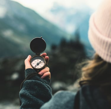 woman's hand holding compass in front of blurry nature backdrop
