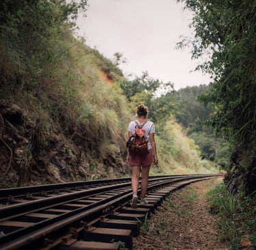 a woman walks along train tracks in a green pass