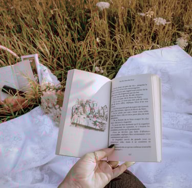 a hand holds a book over a field with wildflowers