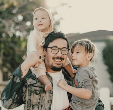 father smiles holding his two young children