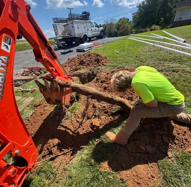 excavator digging up log with man helping