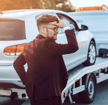 carro ao fundo em cima do guincho sendo apreendido e seu dono na frente preocupado