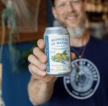 a man holding a can of  soda by wonders of nature.