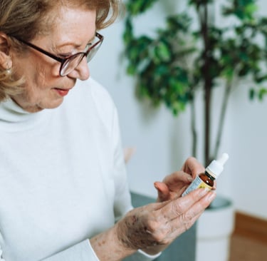 a woman in a white sweater and glasses is holding a bottle of CBD