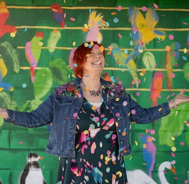 Lady stood in front of a colourful background smiling throwing confetti into the air.