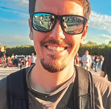 Portrait d’un homme souriant avec des lunettes de soleil reflétant une foule, ciel bleu et ambiance ensoleillée d’événement