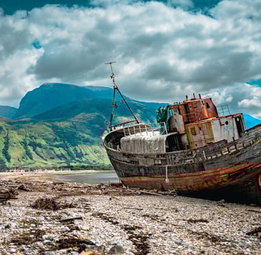 L’épave de Corpach repose sur la plage encadrée par les montagnes imposantes, créant une scène à la fois mystique et paisible
