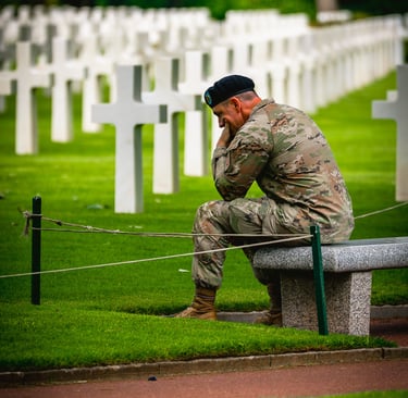 Soldat en uniforme de camouflage assis sur un banc dans un cimetière militaire, exprimant tristesse devant des croix blanches