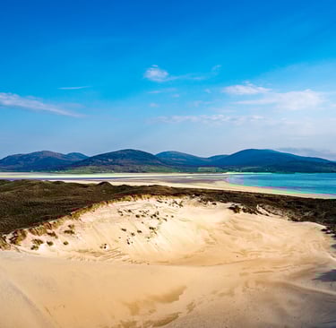 La plage de Luskentyre dévoile ses vastes dunes de sable doré, bordée par une mer turquoise et des montagnes lointaines.