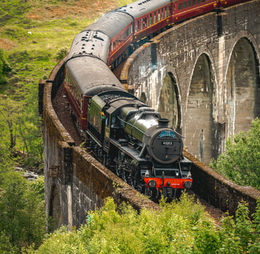 Le train Poudlard Express traverse majestueusement le viaduc de Glenfinnan, entouré de verdure luxuriante.