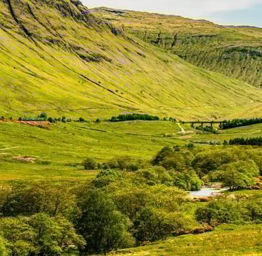 Vallée verdoyante de Glencoe en Écosse, bordée de montagnes majestueuses sous un ciel lumineux et dégagé.