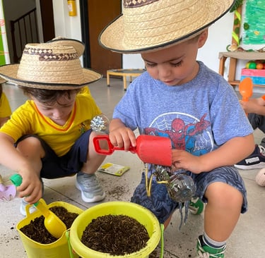 Niños jugando a la jardinería con tierra en baldes amarillos y sombreros campesinos en Jardín infantil Ukelele