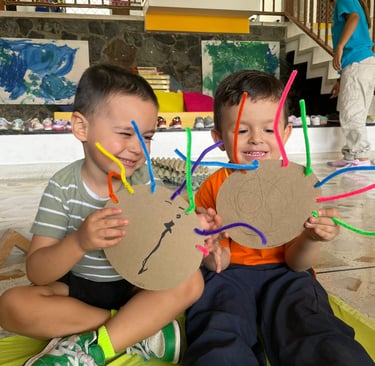 Niños mostrando obras de artes propias hechas con materiales reciclables en jardín Infantil Ukelele