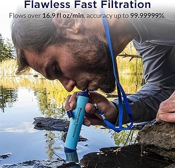 A hiker using a portable water filter straw to drink directly from a natural lake.