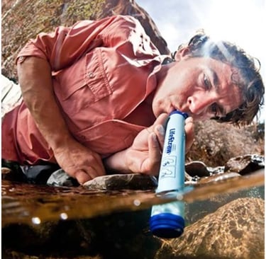 A hiker using a LifeStraw personal water filter to drink directly from a natural stream while outdoors.