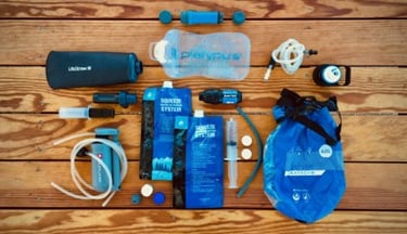 Backpacking water filters and gravity purification systems laid out on a wooden deck.