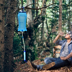 A hiker drinking clean water from a portable gravity water filter bag hanging in the forest.