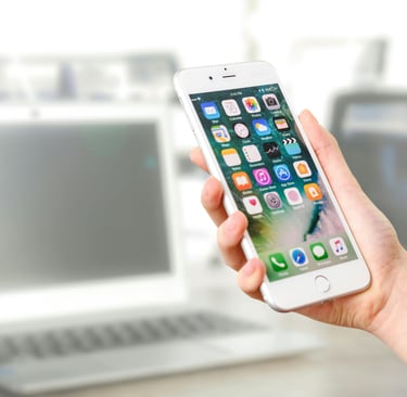 A person holding a cell phone in their hand and computers in the background