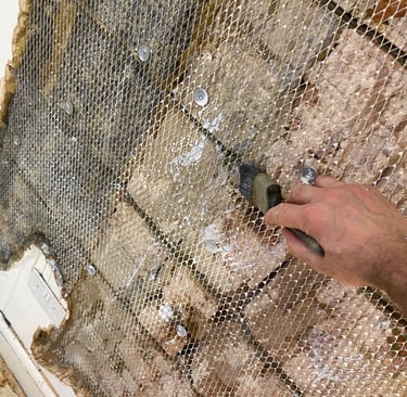 Hand applying bonding agent with a brush onto metal lath mesh for a masonry wall repair.
