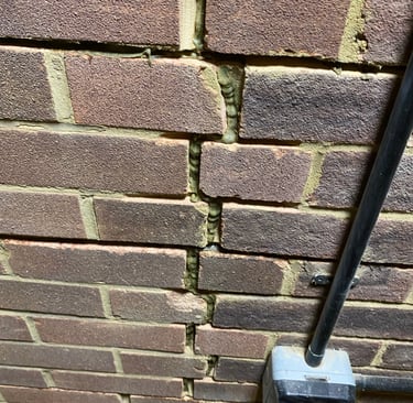 Vertical crack in a residential brick wall showing structural damage and signs of old mortar repair.