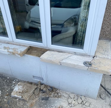 Damaged stone window sill requiring repair on a residential house exterior with debris on the ground.