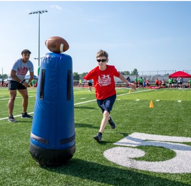 A young boy in a red t-shirt running through football drills with a coach on a turf field.