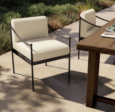 Modern black metal outdoor dining chairs with cream cushions on a stone patio by a wooden table.