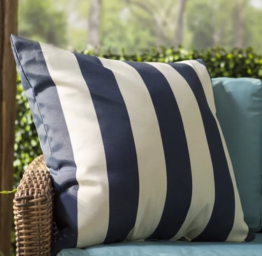Navy blue and white striped outdoor decorative pillow on a wicker patio chair with teal cushions.