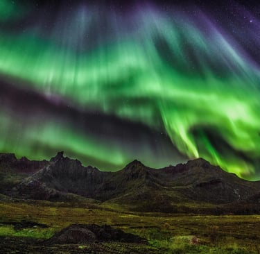 the northern lights appearing in green over a rugged mountainous landscape