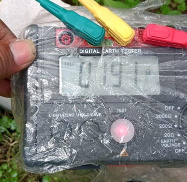 A digital earth tester meter displaying a resistance reading with color-coded test leads attached.